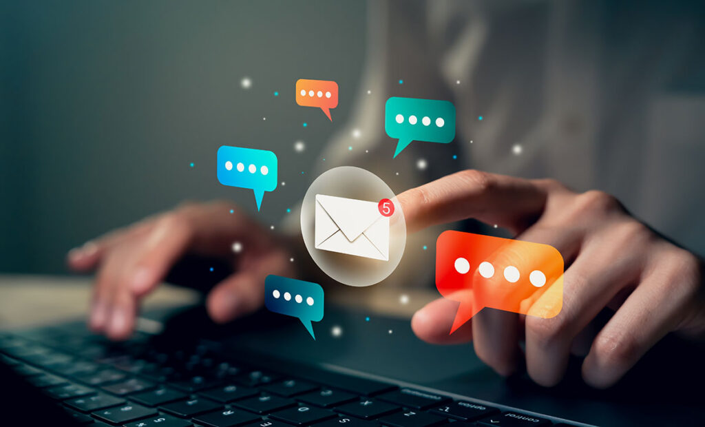 Hand am Laptop mit mehreren Sprechblasen, E-Mail Icon wird mit dem linken Zeigefinger angeklickt.